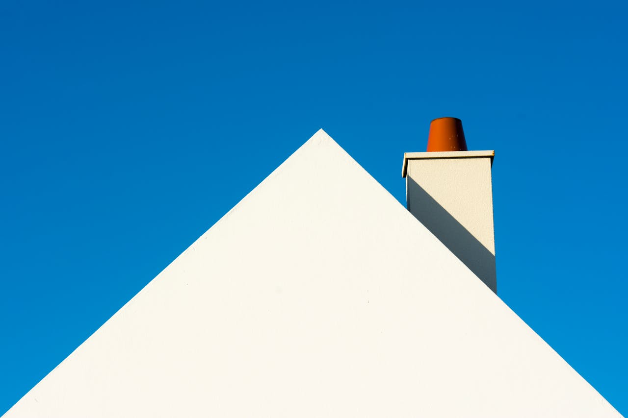 A minimalist photo of a white roof with a chimney against a vibrant blue sky.